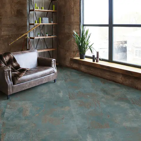 Ambiente con poltrona in pelle e pavimento in gres effetto metallo ossidato verde e bruno